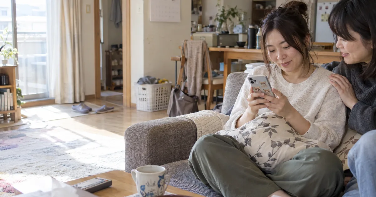 ソファでペットの写真を見る30代の女性と、肩に手を添える友人