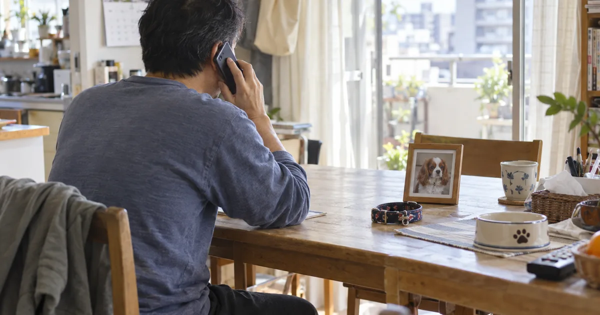 キャバリアの写真と首輪を前に電話をかける40代の男性